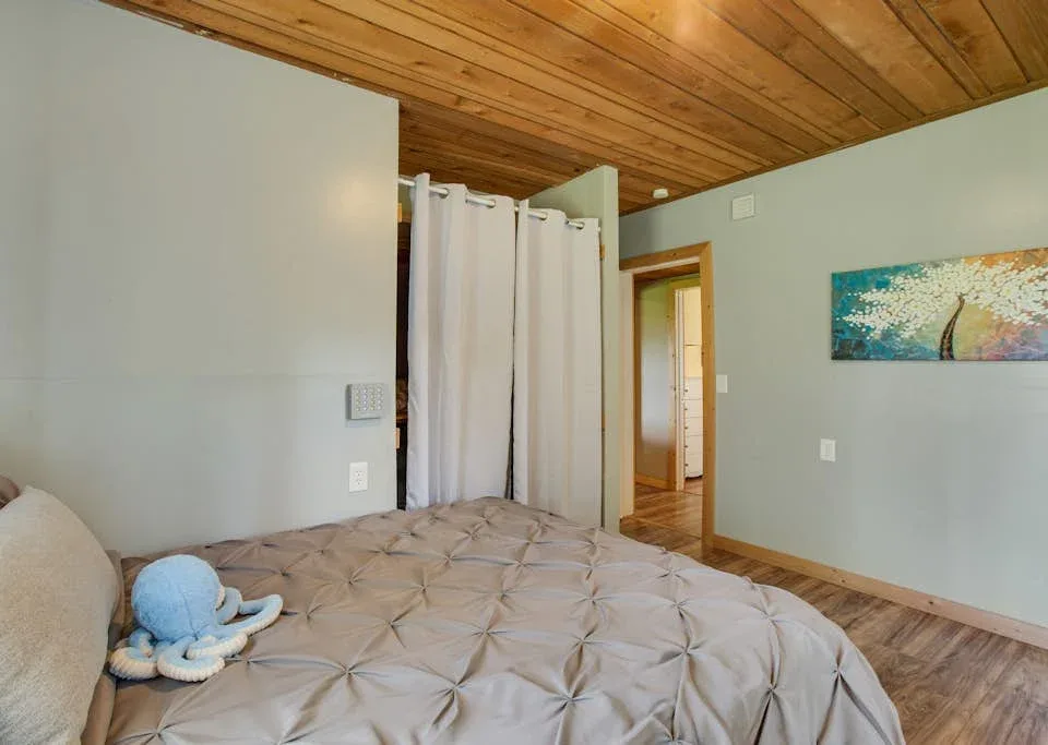 A bedroom with a bed, white curtains, and a wooden ceiling.