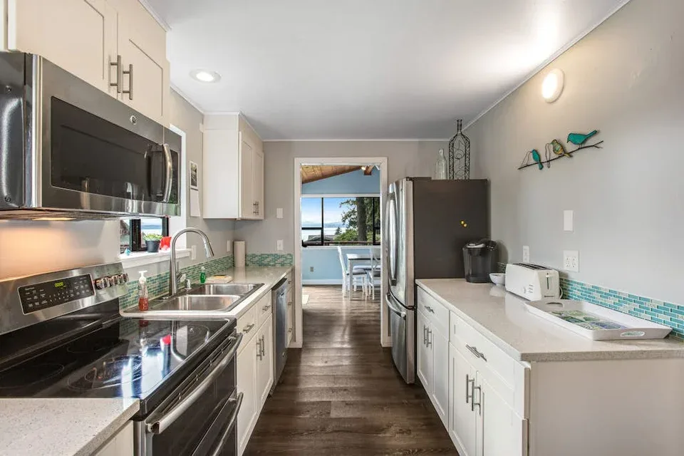 A compact kitchen with white cabinets, stainless steel appliances, and a central walkway.