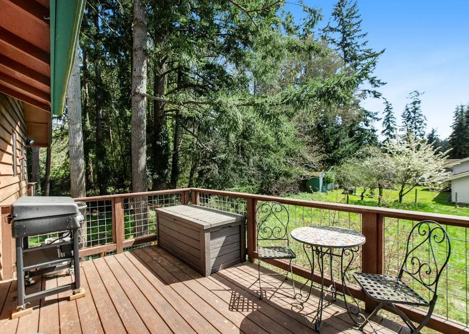 A wooden outdoor deck overlooks a green yard, with a grill and patio seating.