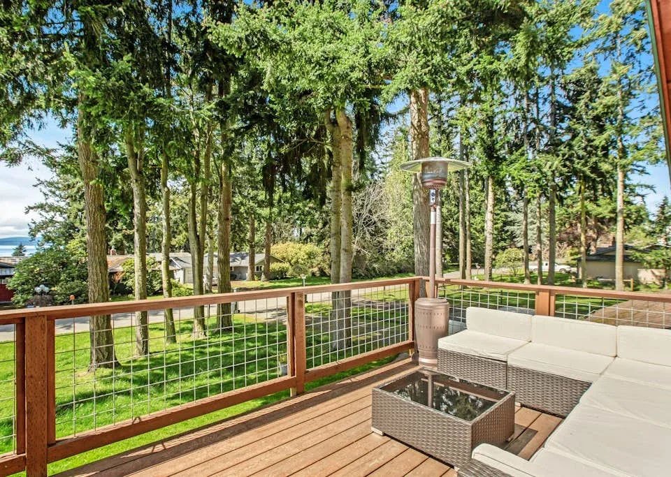 A wooden deck with outdoor seating overlooks a green, tree-filled yard.
