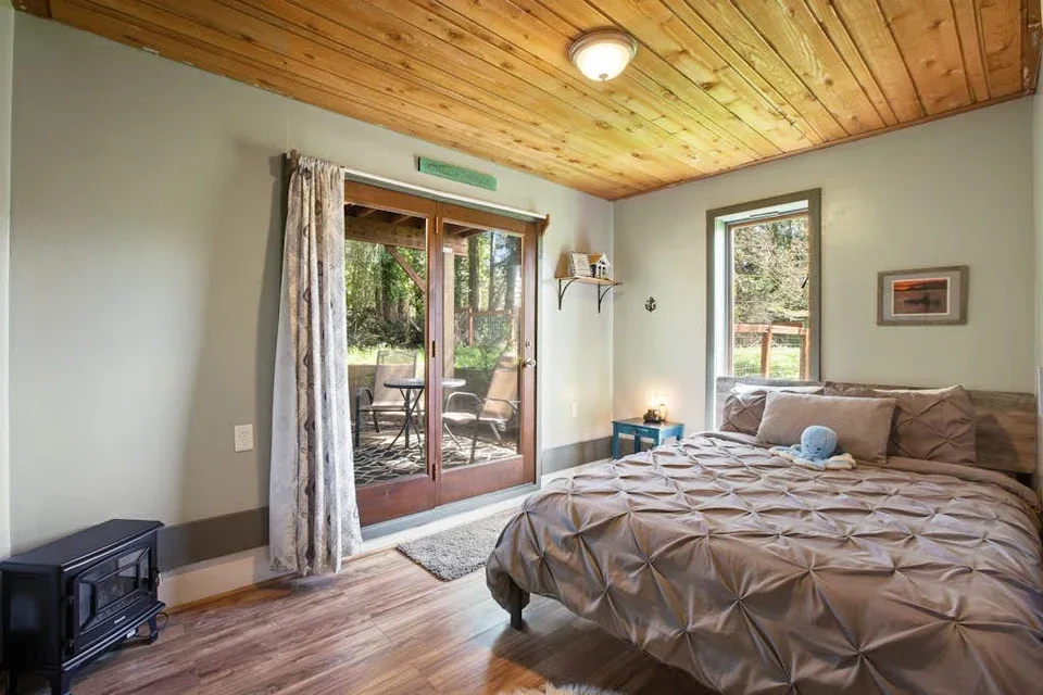 A bedroom with a large bed, a wood-paneled ceiling, and glass doors opening to a patio.