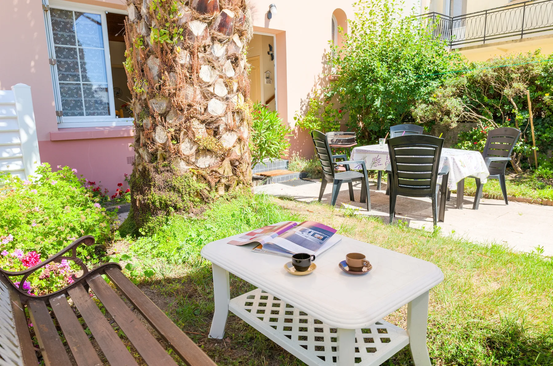 An outdoor patio with tables and seating sits beside a leafy garden.