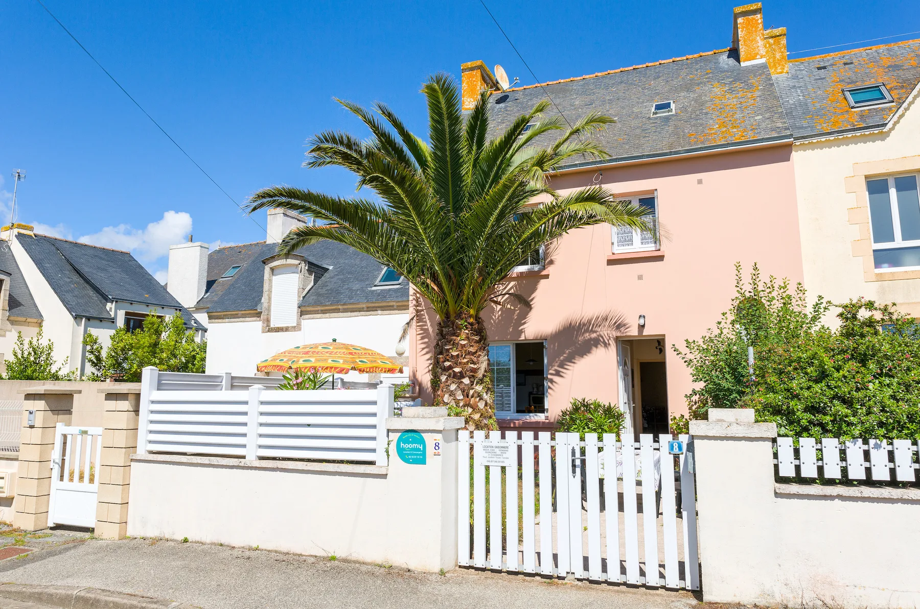 A house behind a white picket gate, with a palm tree in front.