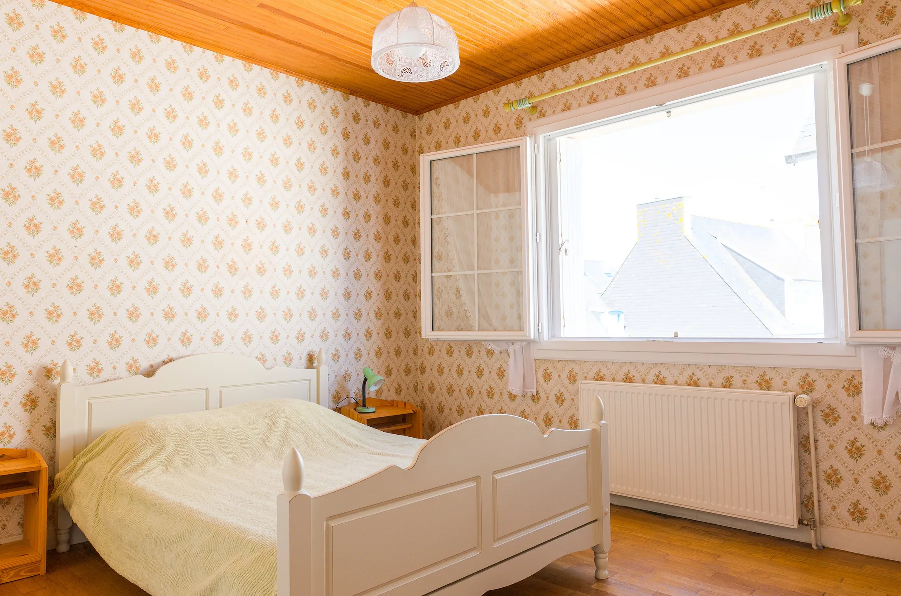 A bedroom with a bed, patterned wallpaper, and a large window.