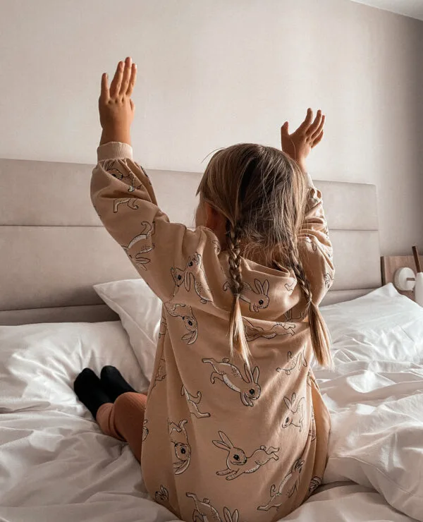 Representative hotel space: A child sits on a bed with both arms raised.