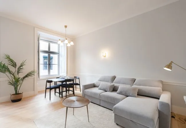 Una sala luminosa con asientos grises, una mesa de centro y un comedor junto a la ventana.