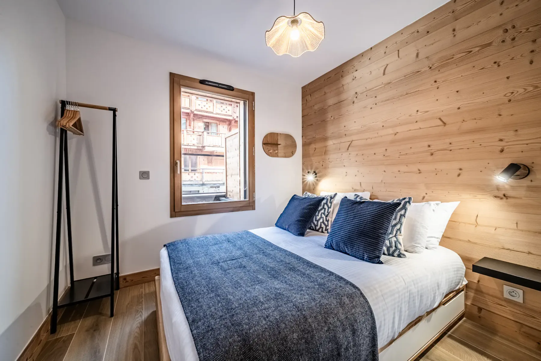 Un dormitorio con una cama vestida de blanco y azul junto a una pared revestida de madera.