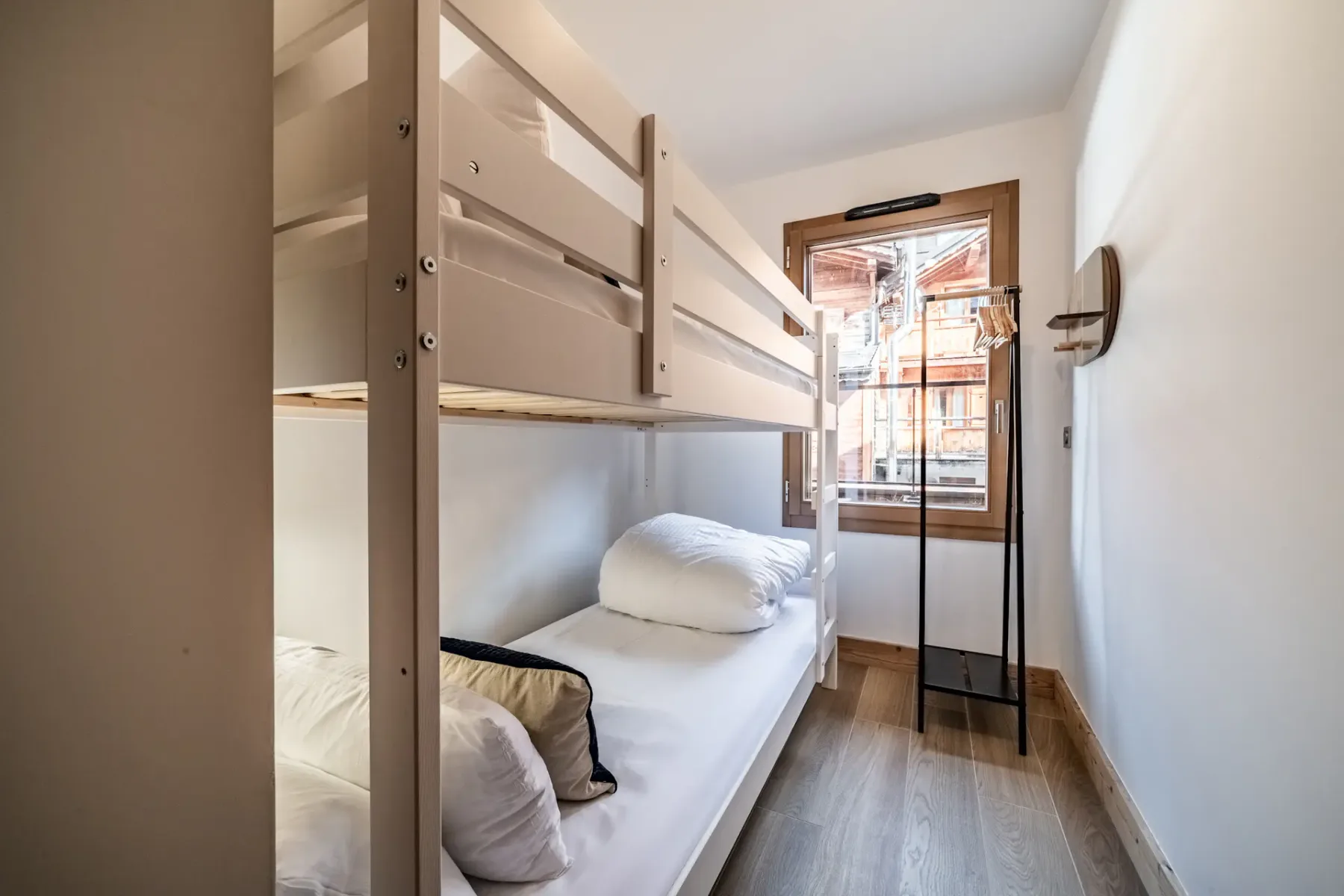 Un dormitorio estrecho con literas y una ventana al fondo.
