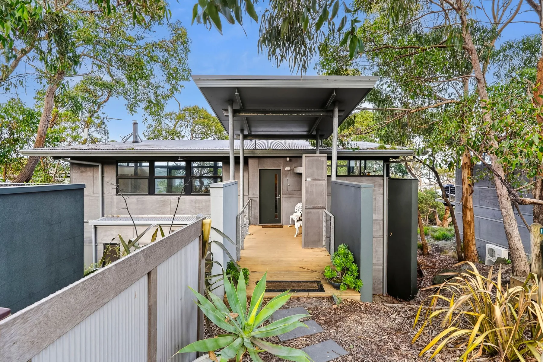 A modern building entrance is reached by a short walkway through leafy landscaping.