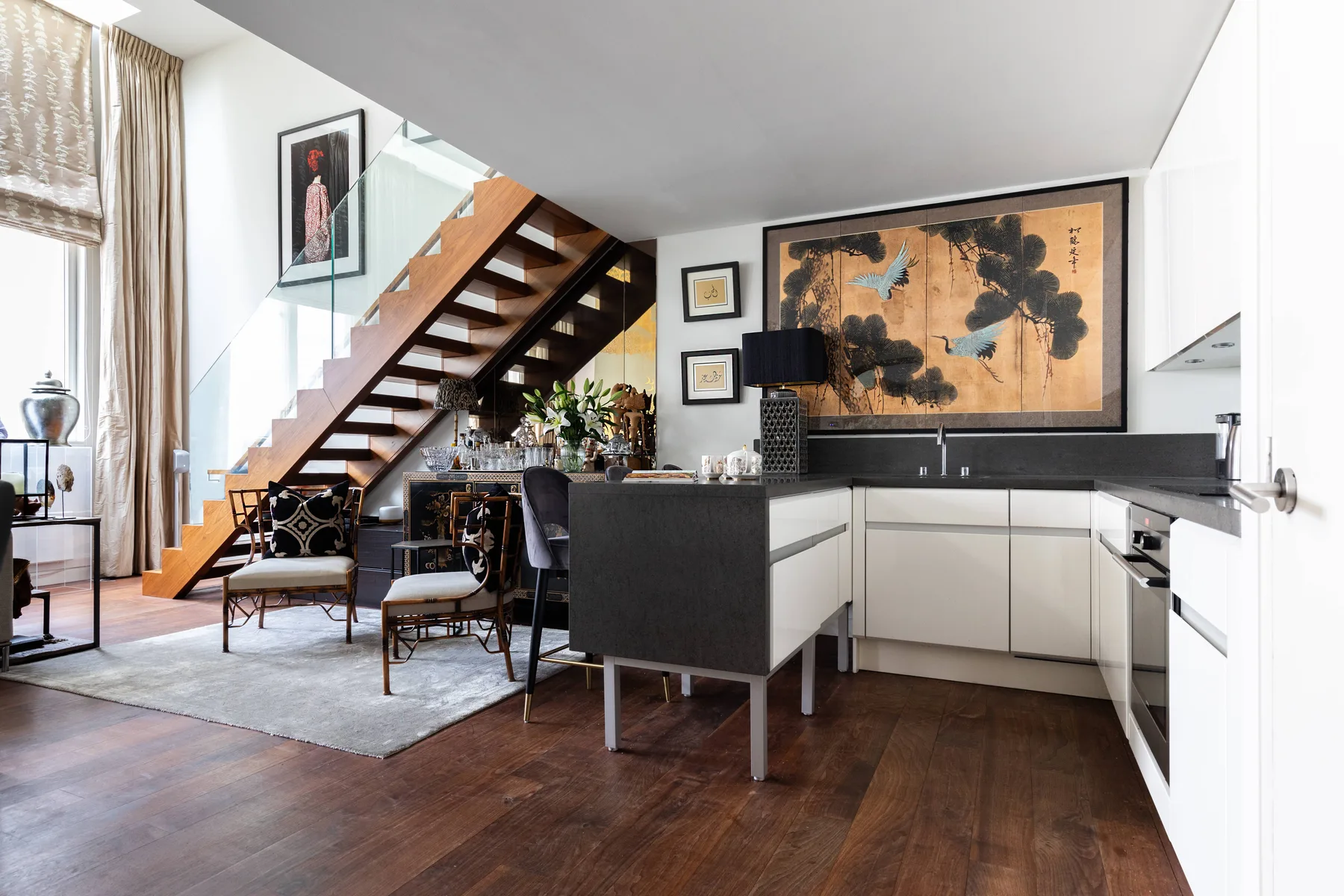 An open-plan kitchen and dining area sits beneath a staircase, with a large framed artwork on the wall.