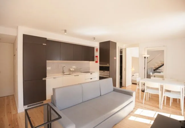 Una sala de estar de planta abierta con sofá gris, cocina y mesa de comedor.