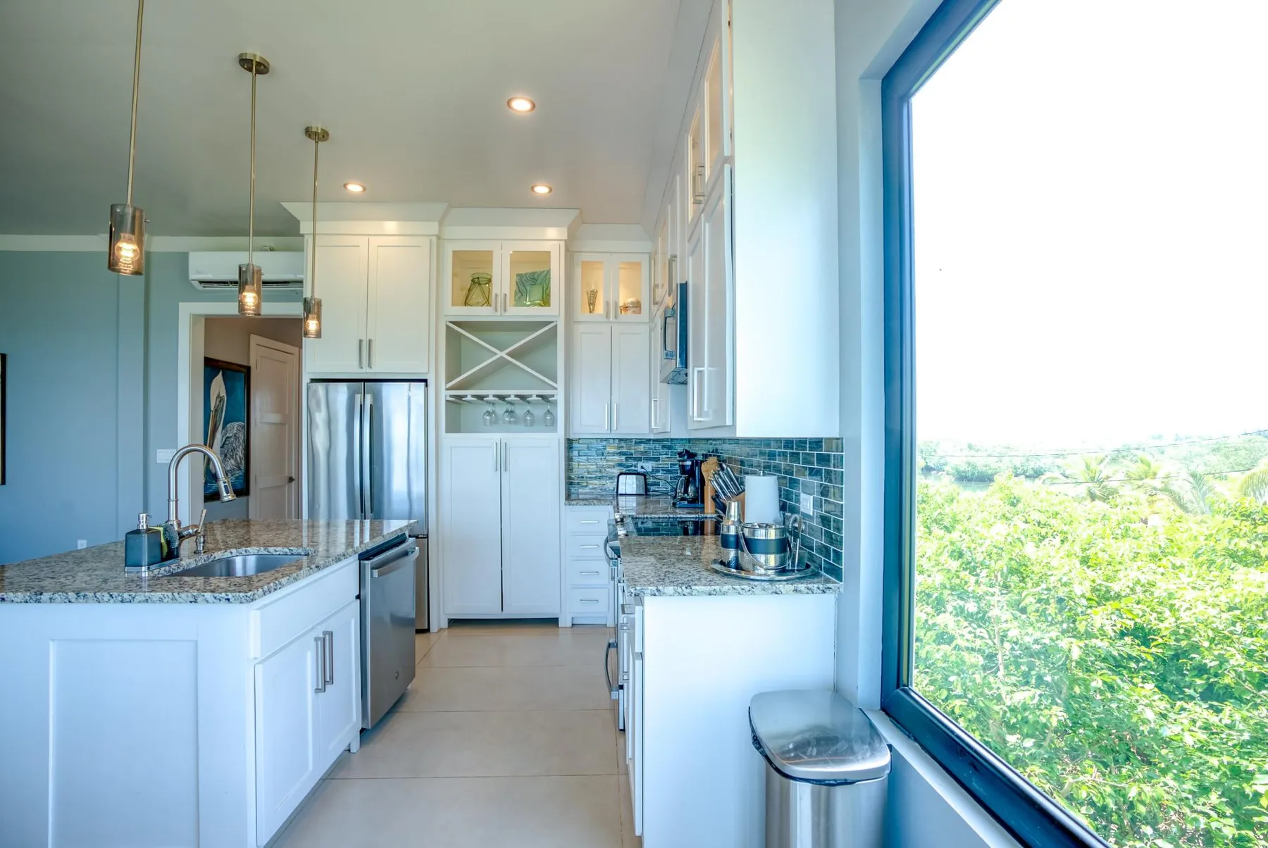 A bright kitchen with white cabinetry, stainless steel appliances, and a large window.