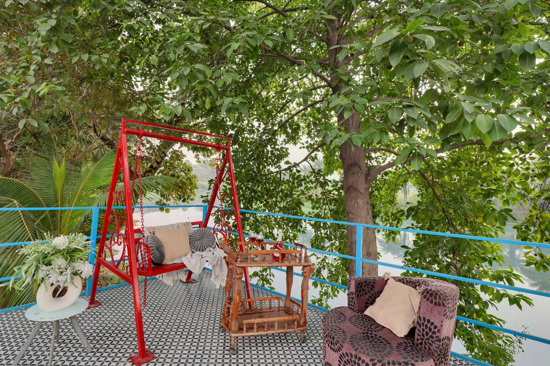 A leafy outdoor seating area has patterned chairs, a small table, and a red swing.