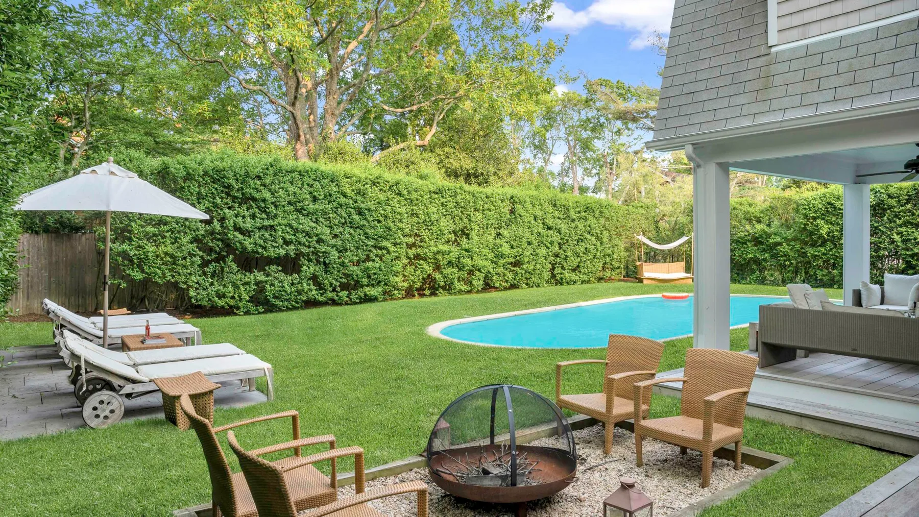 Un patio y césped dan a una piscina, con asientos al aire libre cerca.