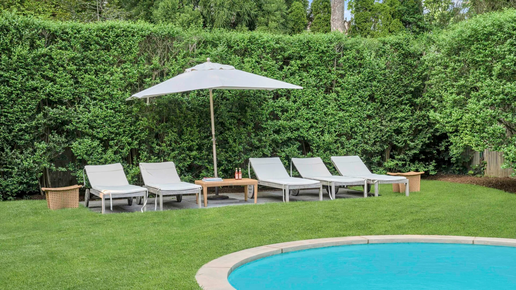 Una piscina al aire libre junto a asientos en el césped y una sombrilla grande.