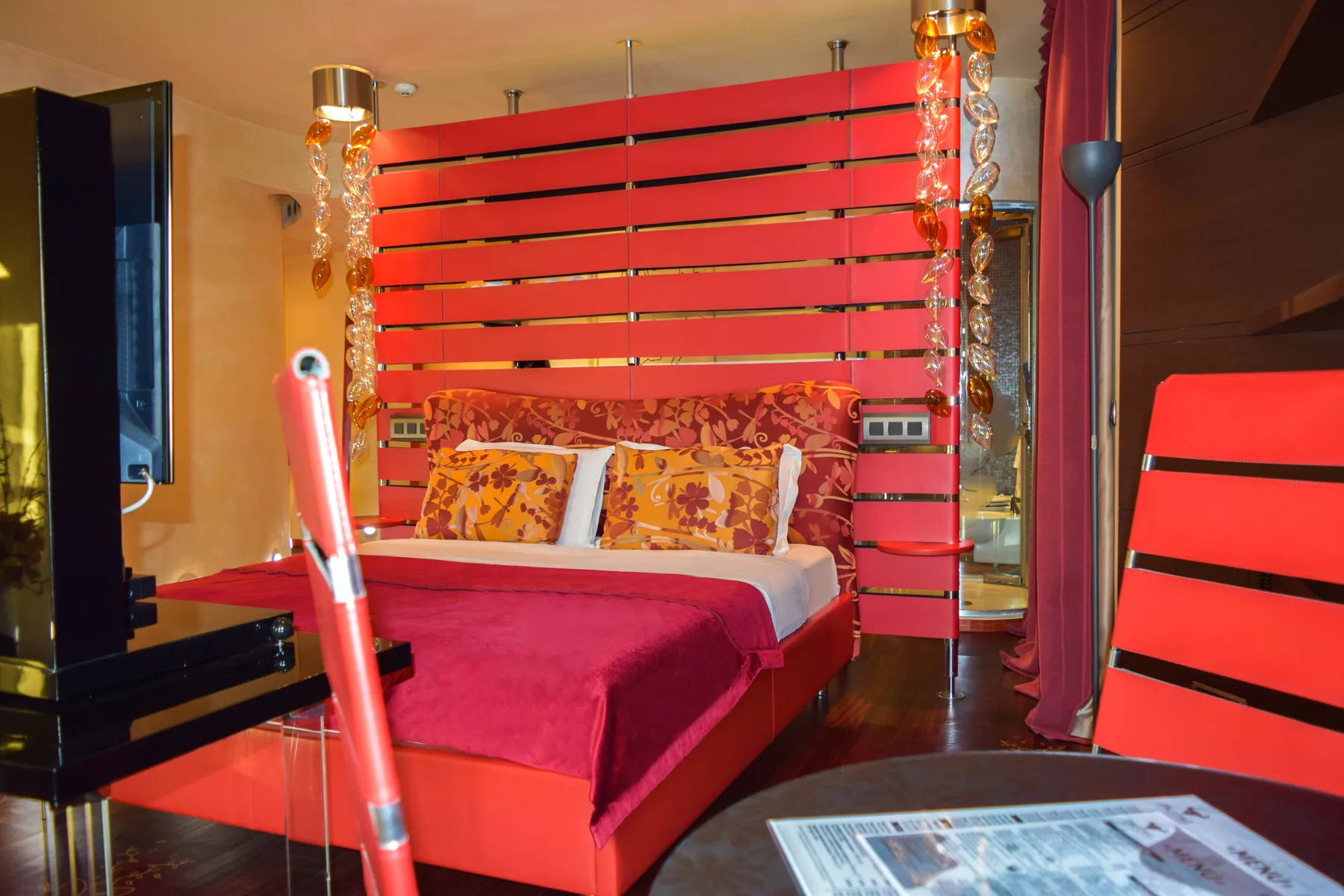 Representative hotel space: A bedroom with a red bed and a slatted divider behind it.