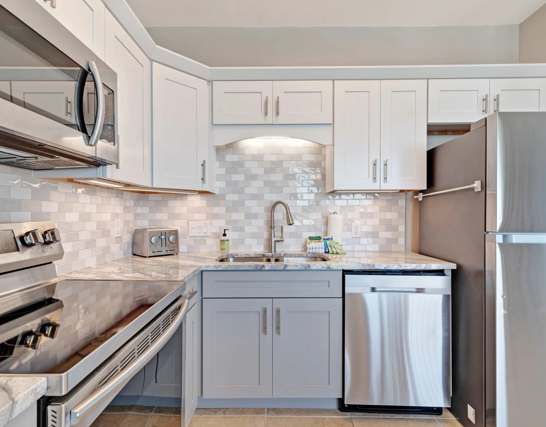 Una cocina luminosa con gabinetes blancos, salpicadero de azulejos y electrodomésticos de acero inoxidable.