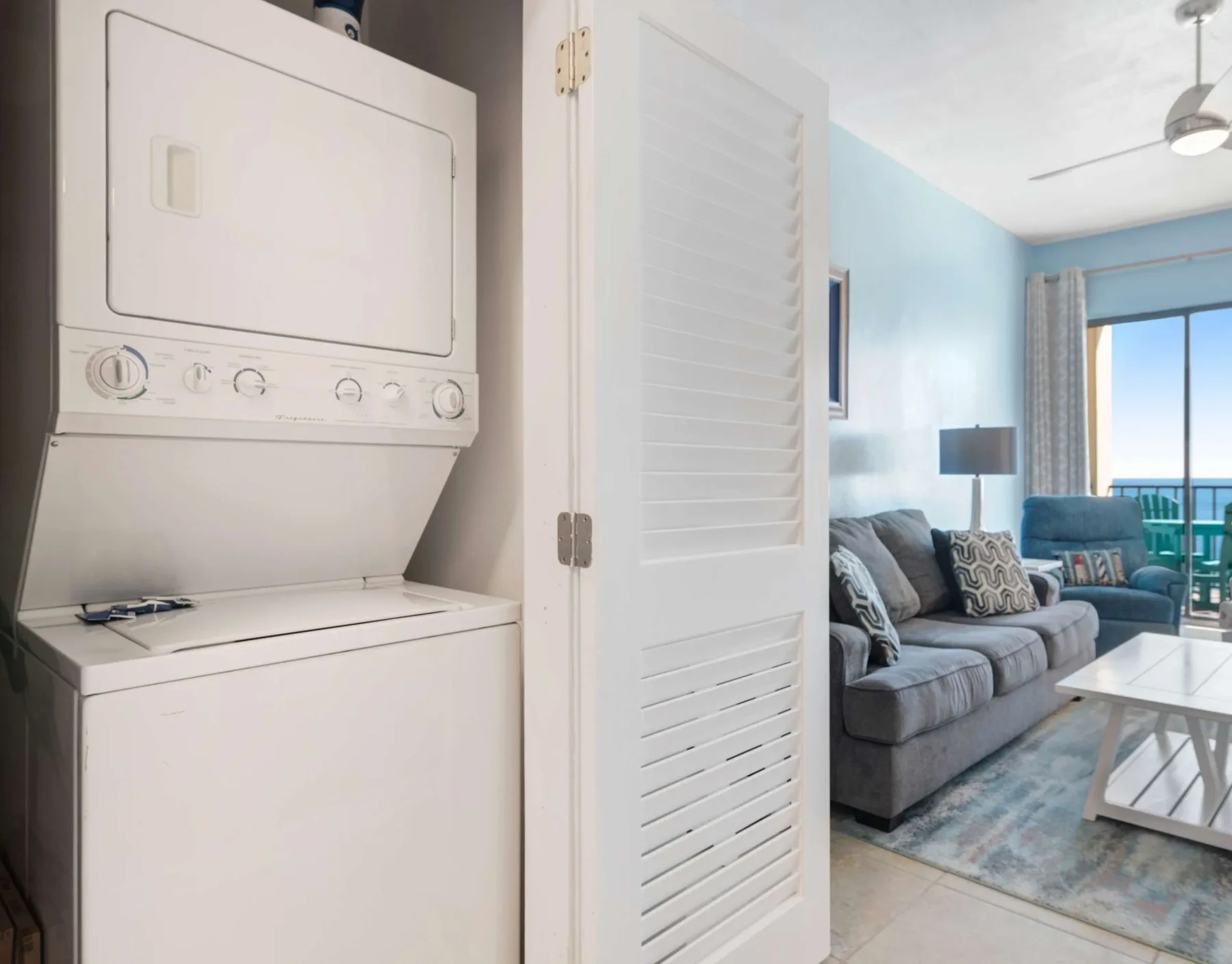 Zona de lavandería con lavadora y secadora apiladas junto a una sala de estar.