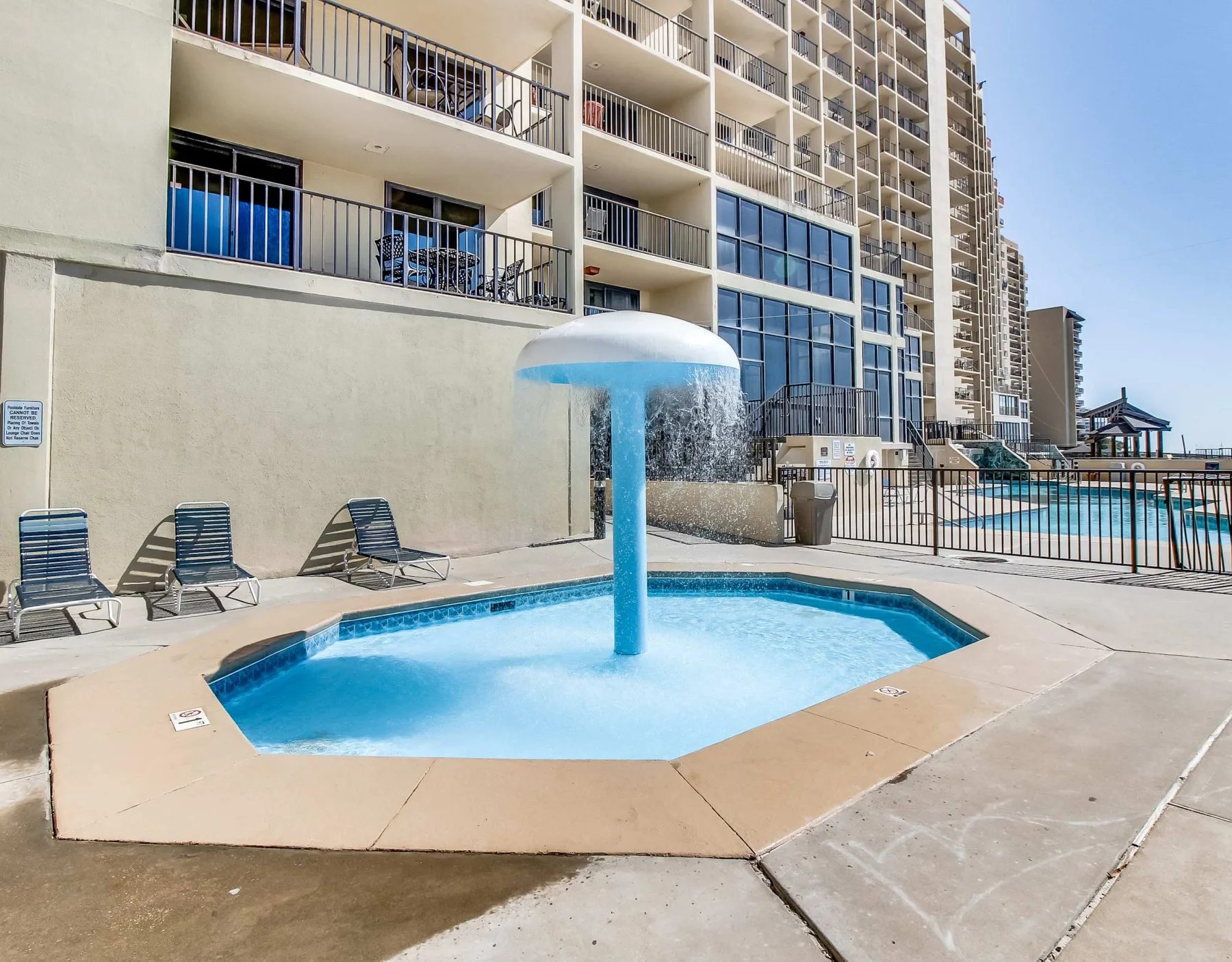 Zona común: Una piscina al aire libre con una fuente en forma de hongo está junto a un edificio alto.