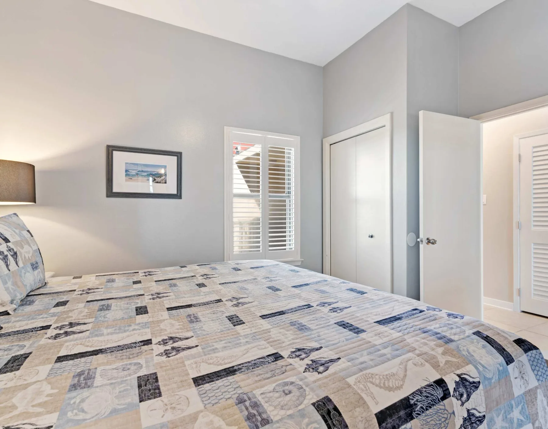 Un dormitorio con una colcha estampada y ventanas con persianas.