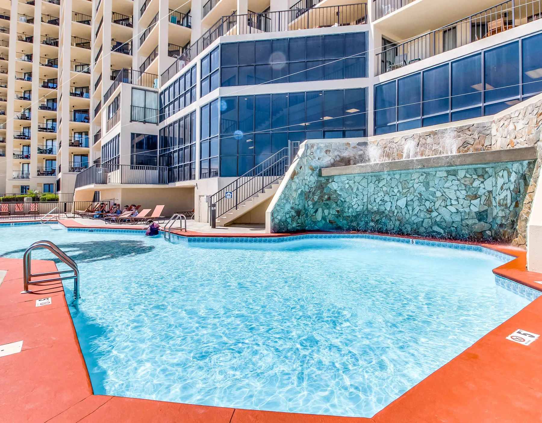 Zona común: Una piscina al aire libre está junto a un edificio moderno con balcones de vidrio.