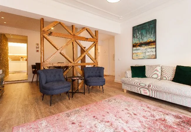 A living room with upholstered seating, a patterned rug, and a wooden room divider.