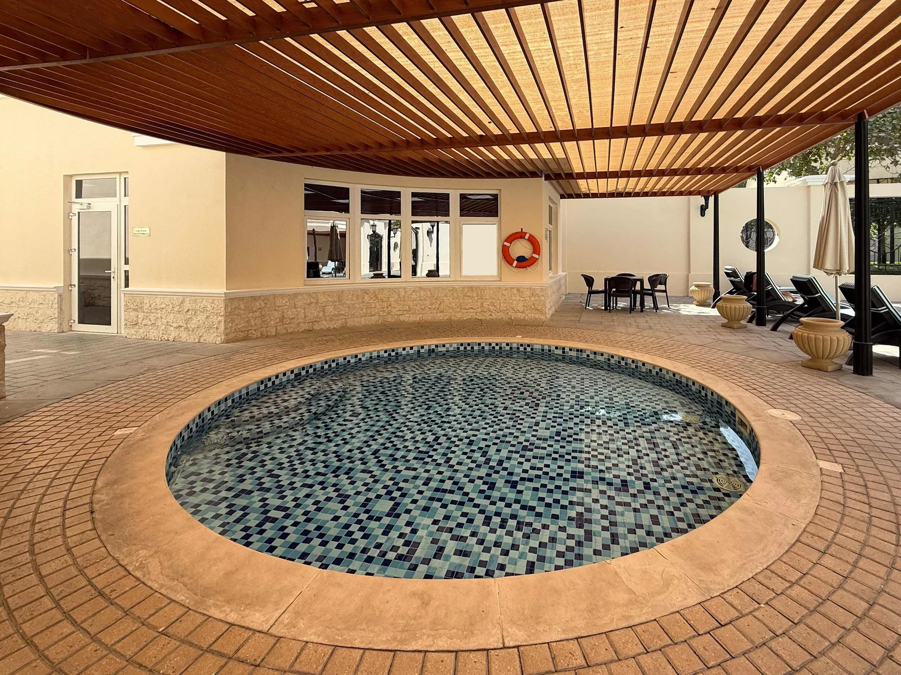 Zona común: Zona de piscina cubierta con una piscina circular revestida de azulejos bajo una pérgola de madera.
