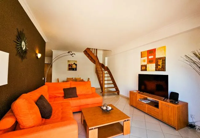 A living room with orange seating, a coffee table, and a television.