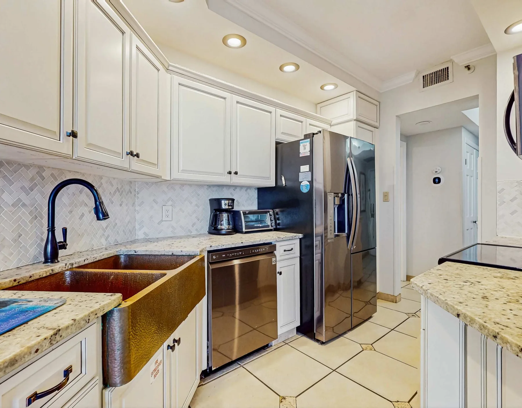 A bright kitchen with white cabinets, stone counters, and stainless steel appliances.
