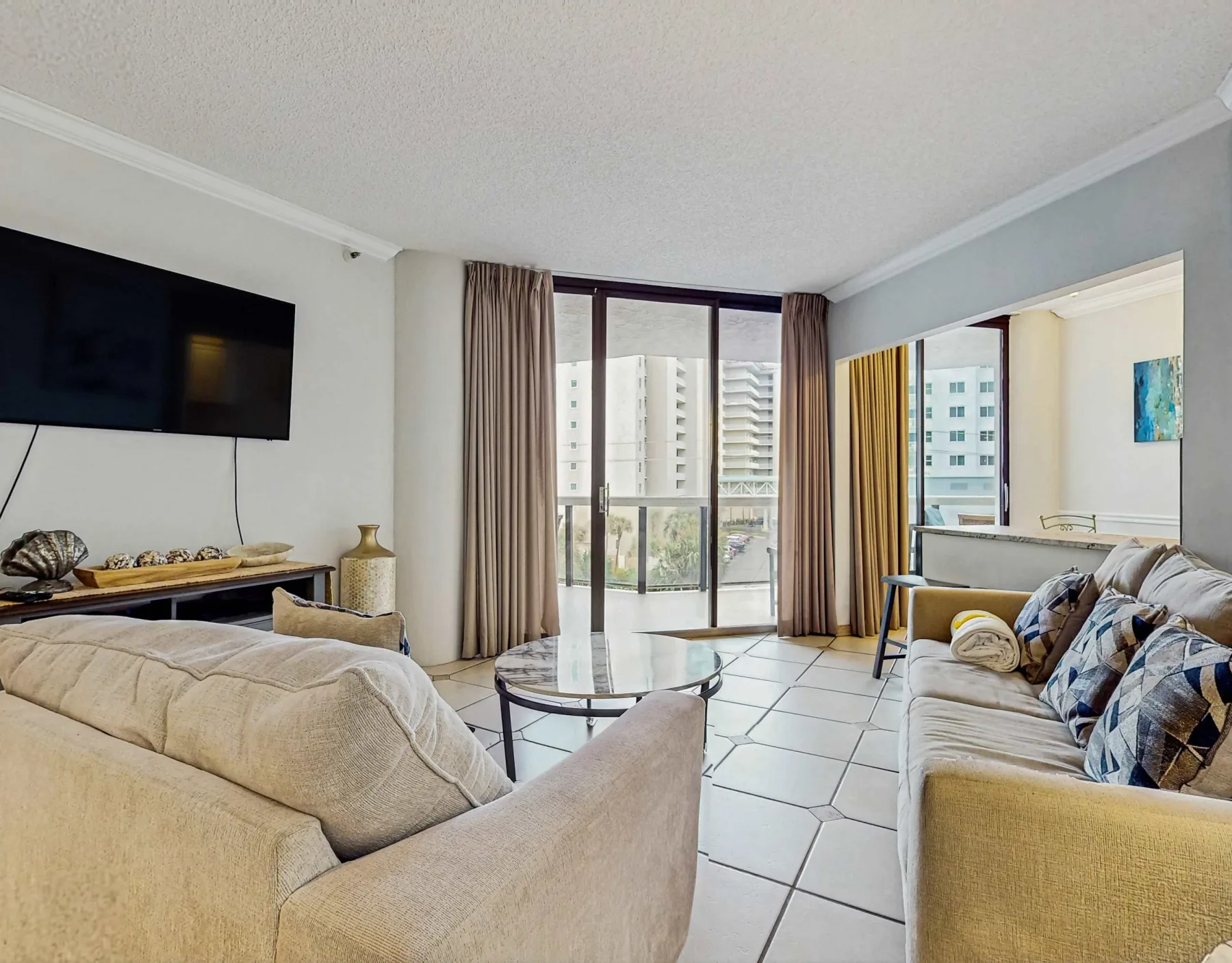 A bright living room with sofas, a glass coffee table, and sliding doors opening onto a balcony.