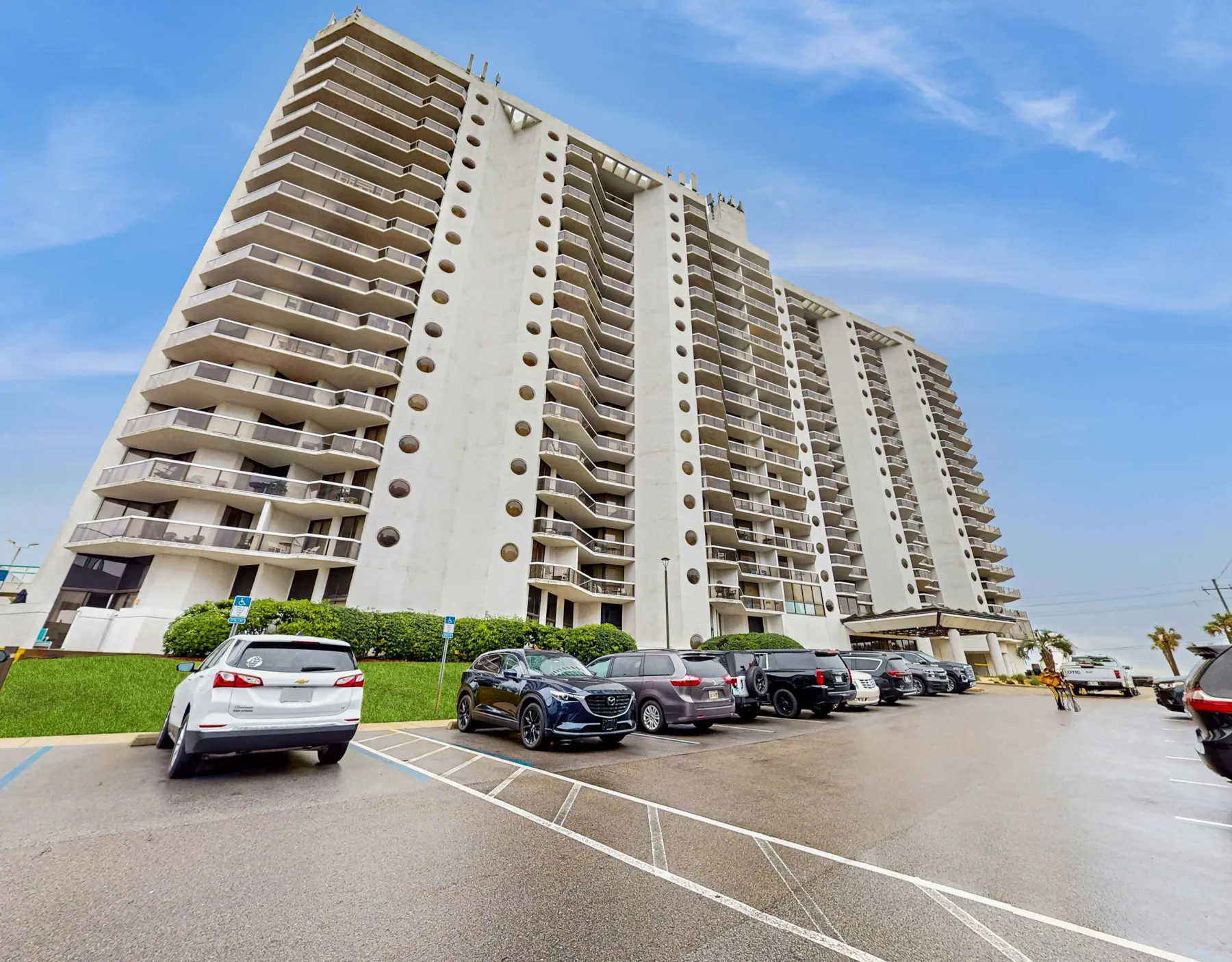 Shared amenity: A high-rise residential building stands beside a parking area with several cars.