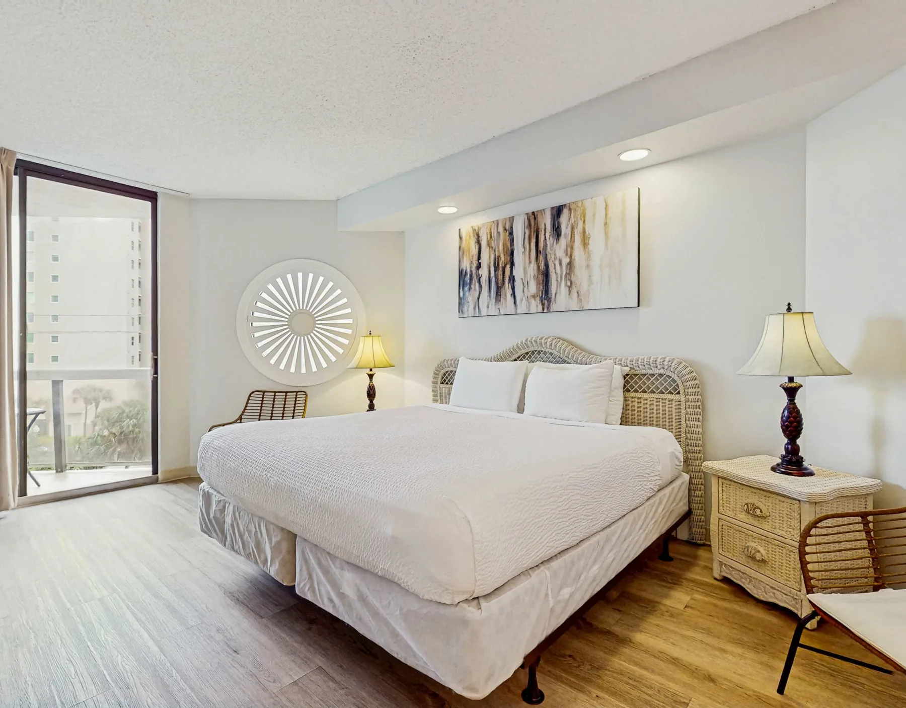 A bright bedroom with a large bed, bedside tables, and abstract wall art.