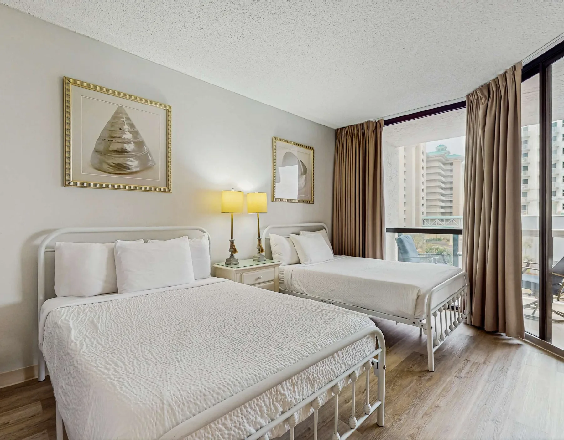 A bedroom with two beds, bedside lamps, and large curtained windows.