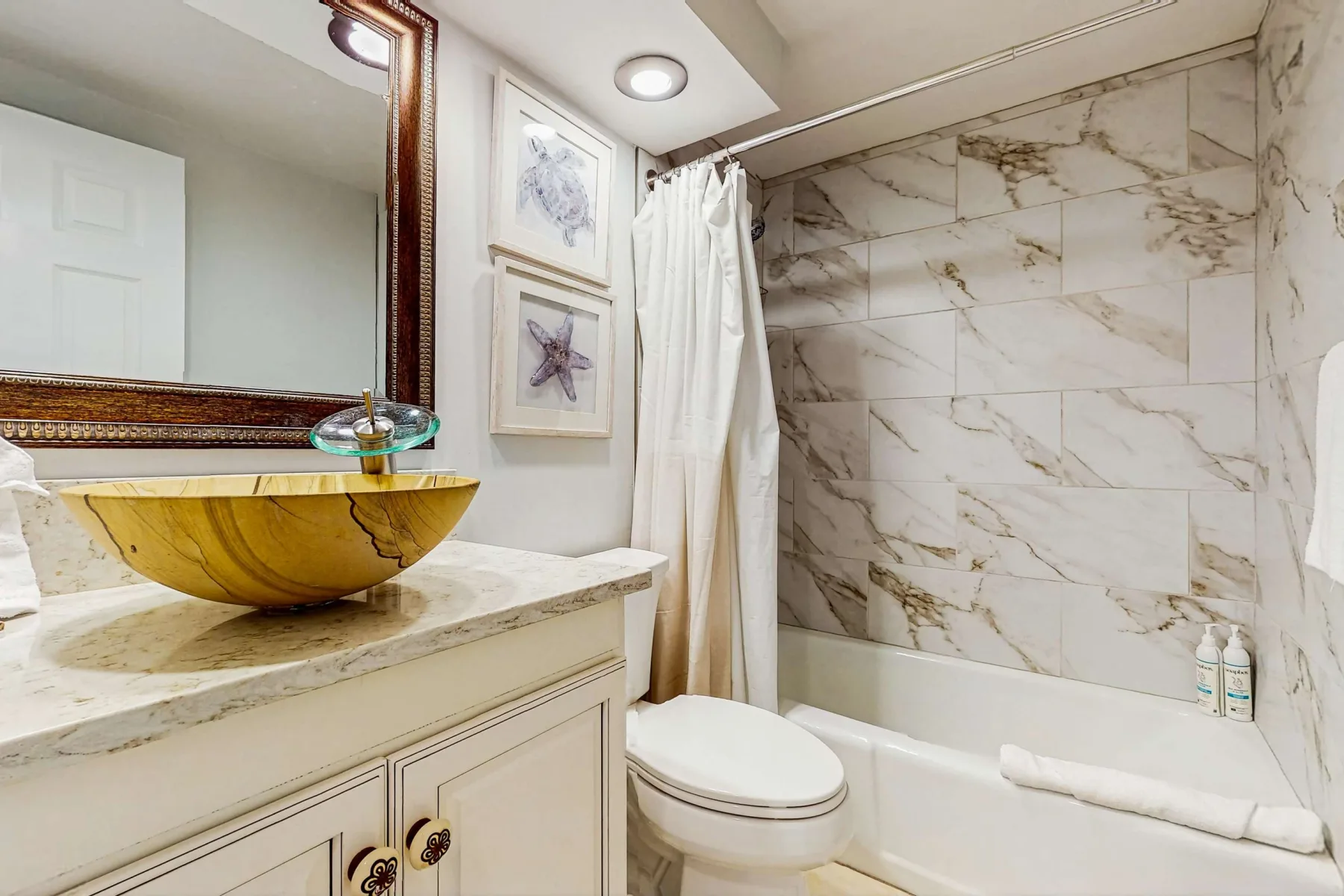 A bathroom with a marble-patterned tub surround and a vanity with a vessel sink.
