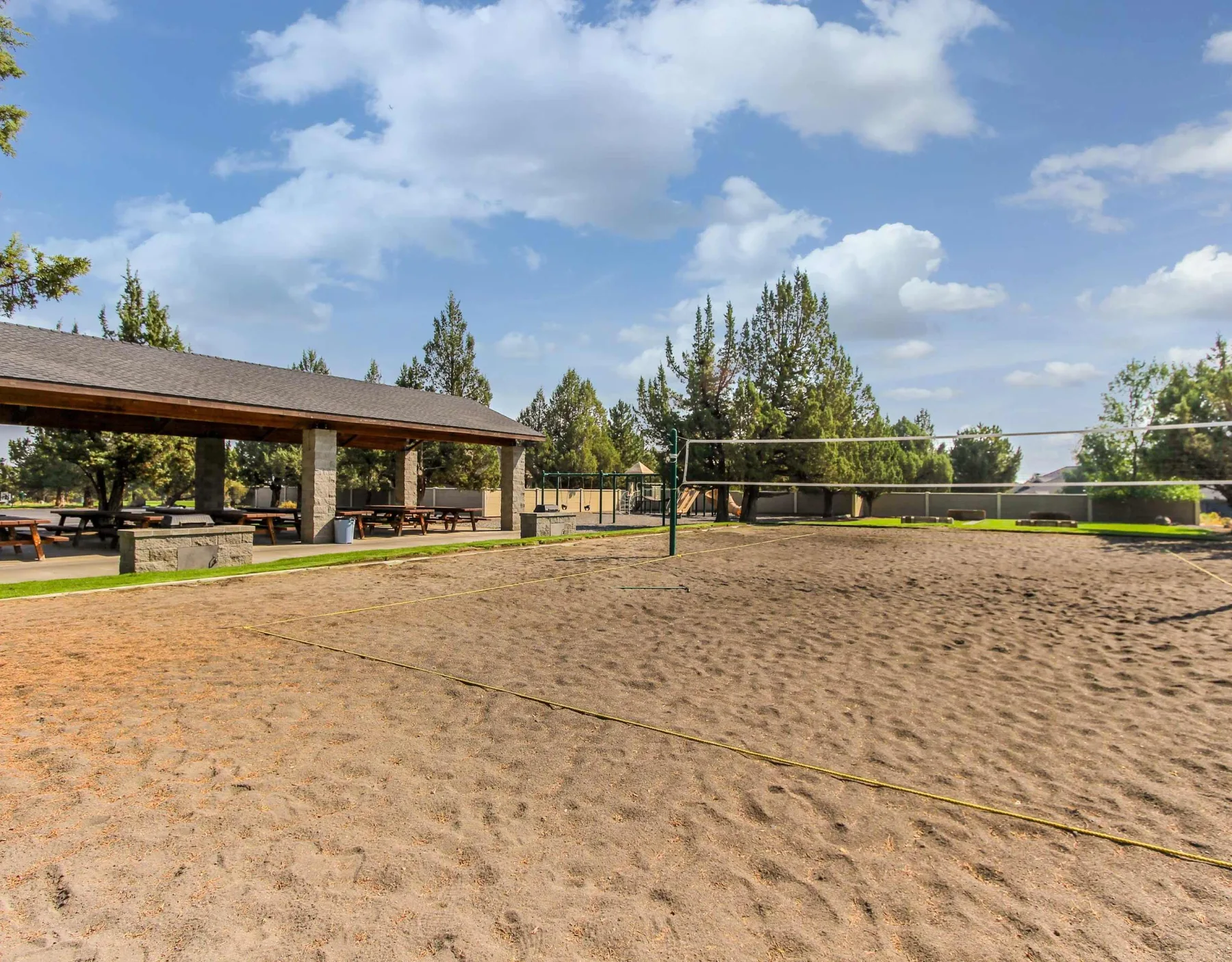 Zona común: Cancha de voleibol al aire libre con arena, junto a una zona cubierta con asientos y árboles.