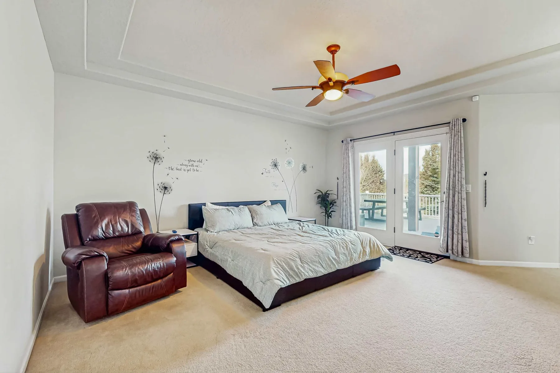 Un dormitorio con una cama grande y un sillón de cuero junto a puertas de vidrio.