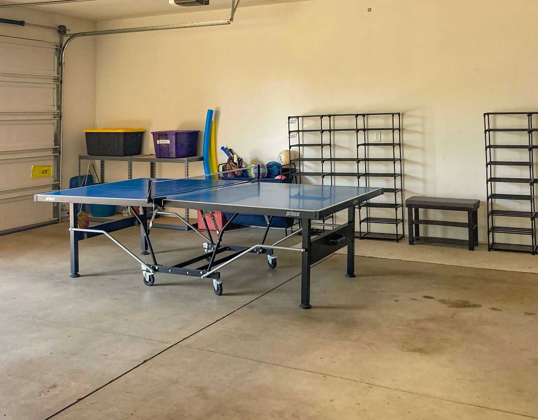 Un garaje preparado para jugar al tenis de mesa, con una mesa y estanterías.