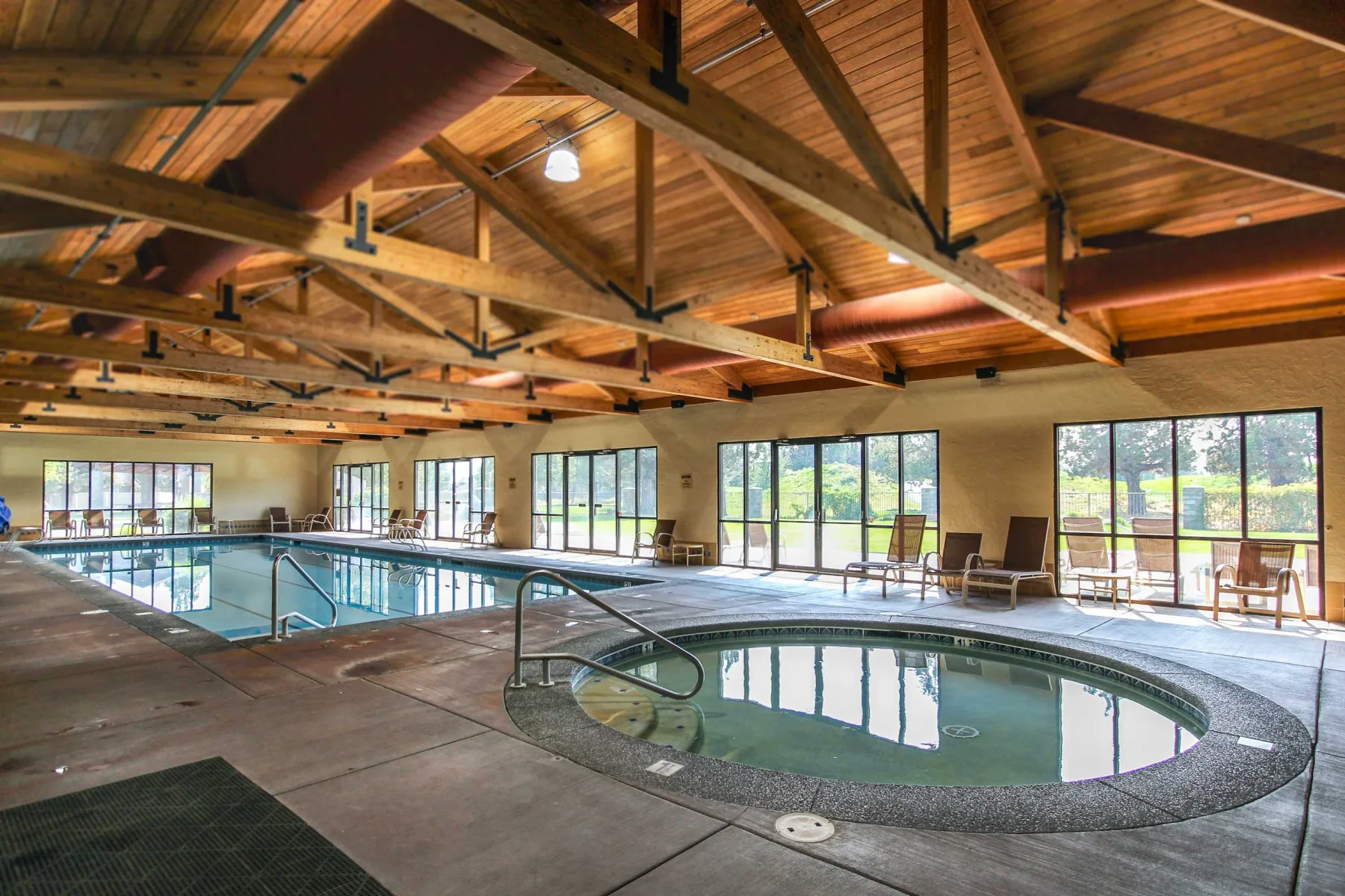 Zona común: Zona de piscina cubierta bajo un techo alto de madera, con grandes ventanas en las paredes.