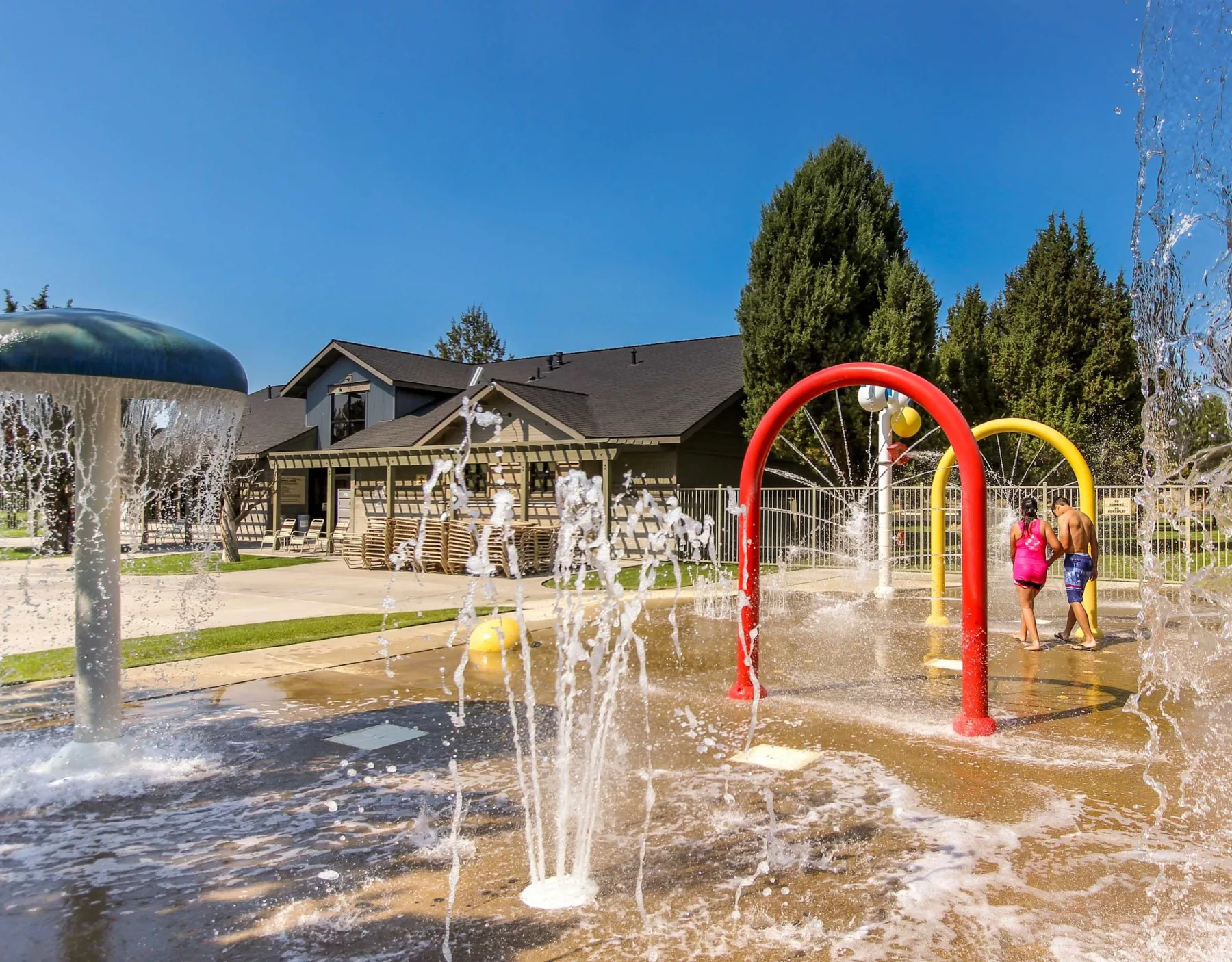 Zona común: Área de juegos acuáticos al aire libre con arcos de agua y personas jugando.