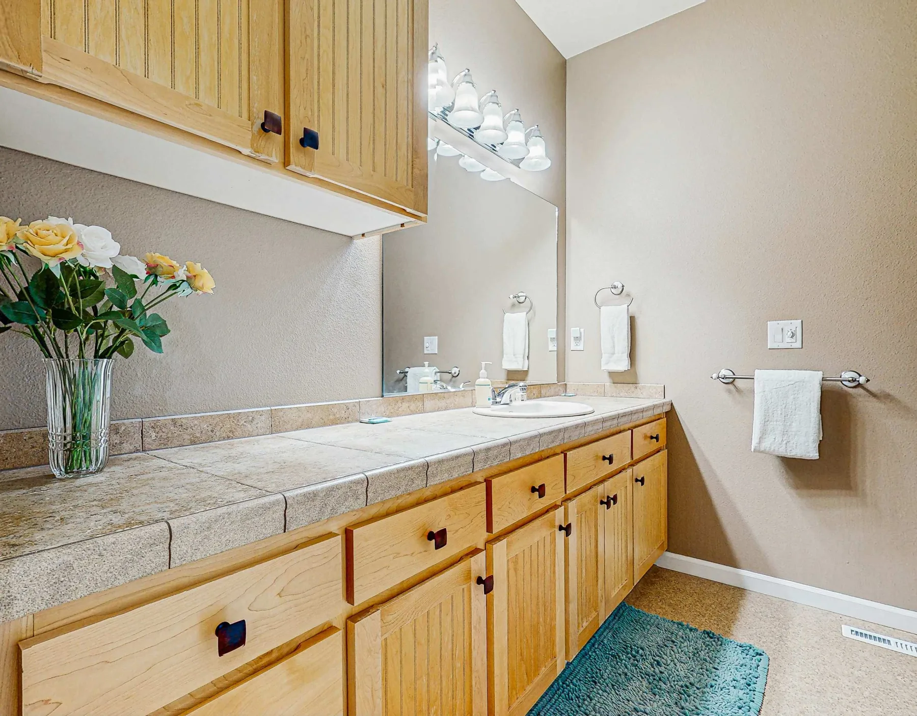 Un tocador de baño con encimera de azulejos, lavabo, espejo y gabinetes de madera.