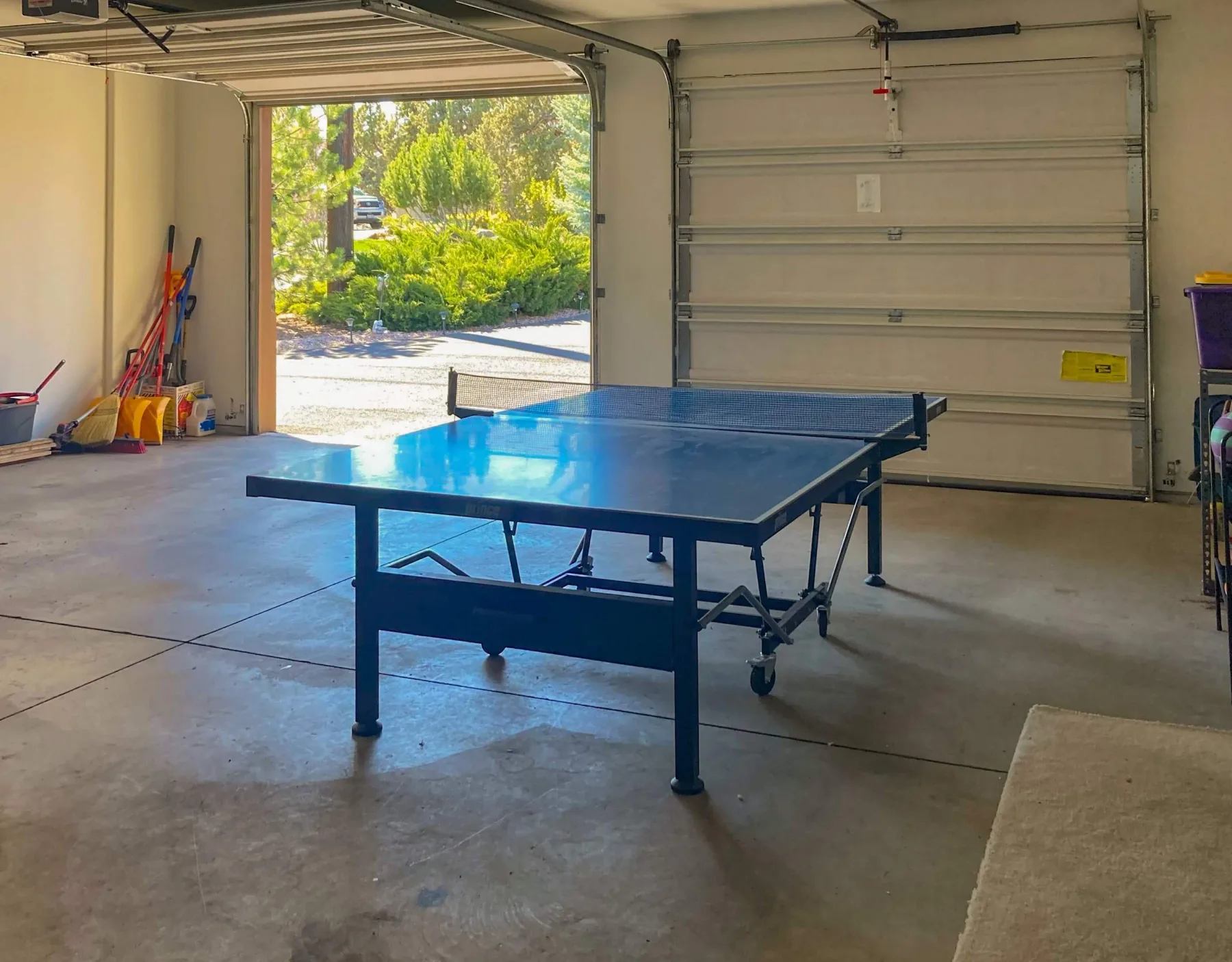 Un garaje con una mesa de tenis de mesa azul y la puerta abierta al exterior.