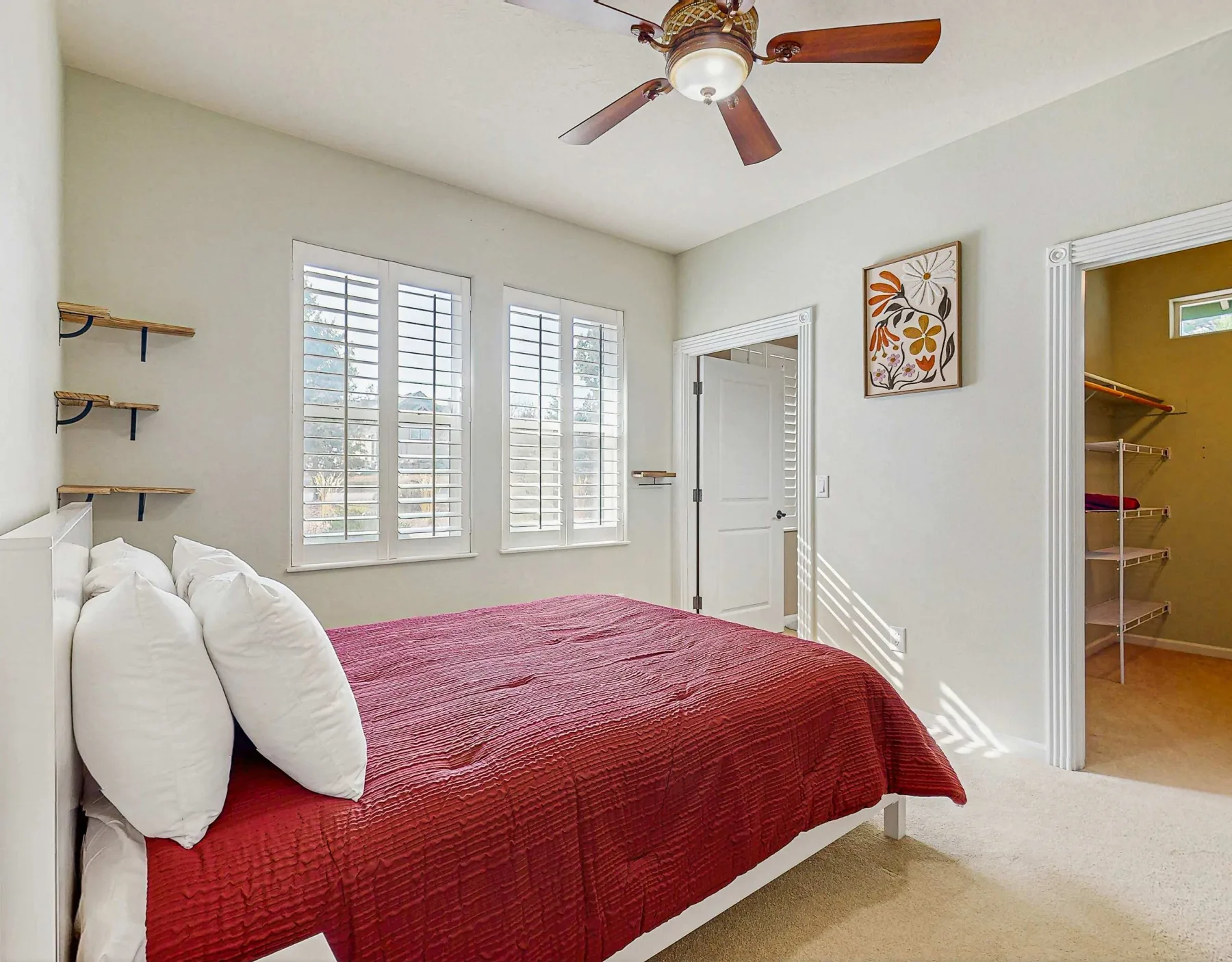 Un dormitorio con una cama cubierta con ropa de cama roja y ventanas con persianas.