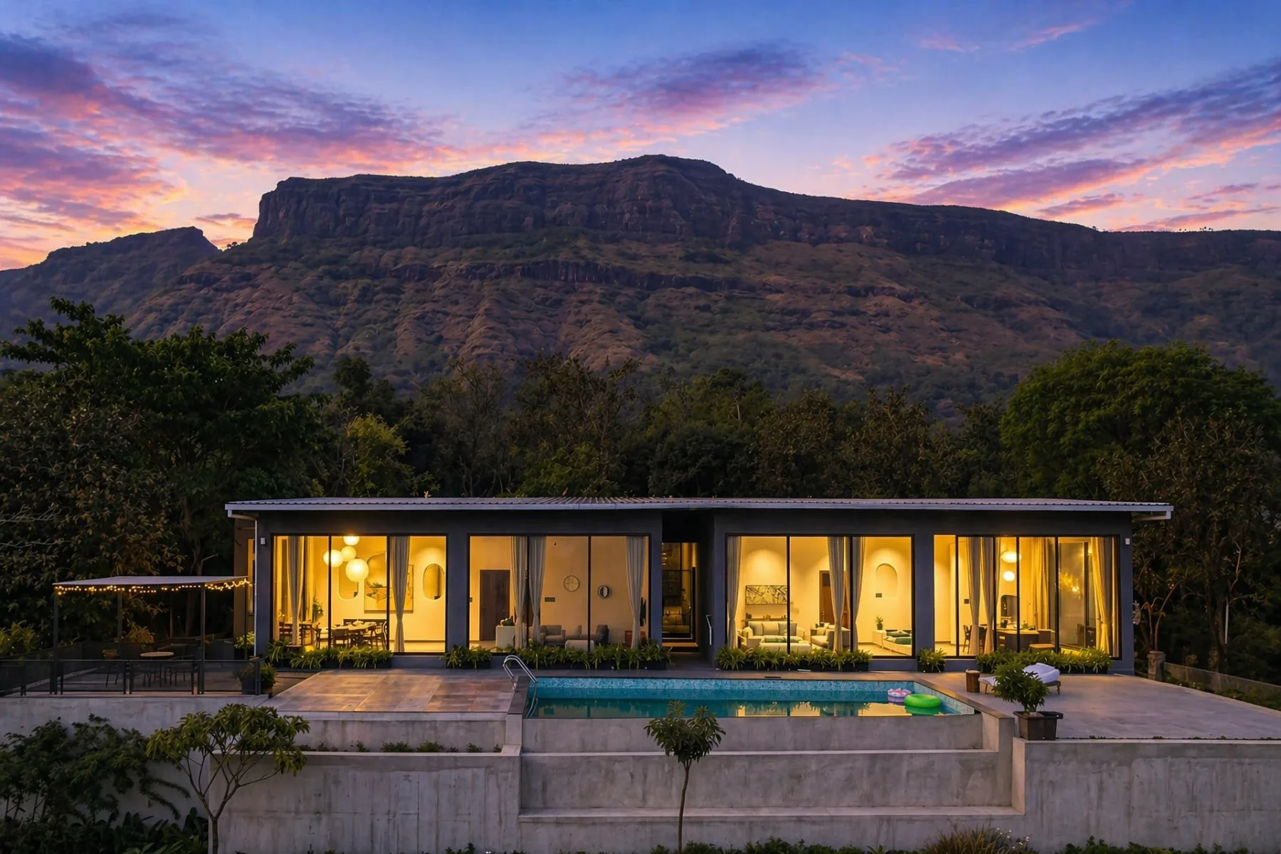 Una casa moderna se ilumina bajo una cresta montañosa al atardecer.