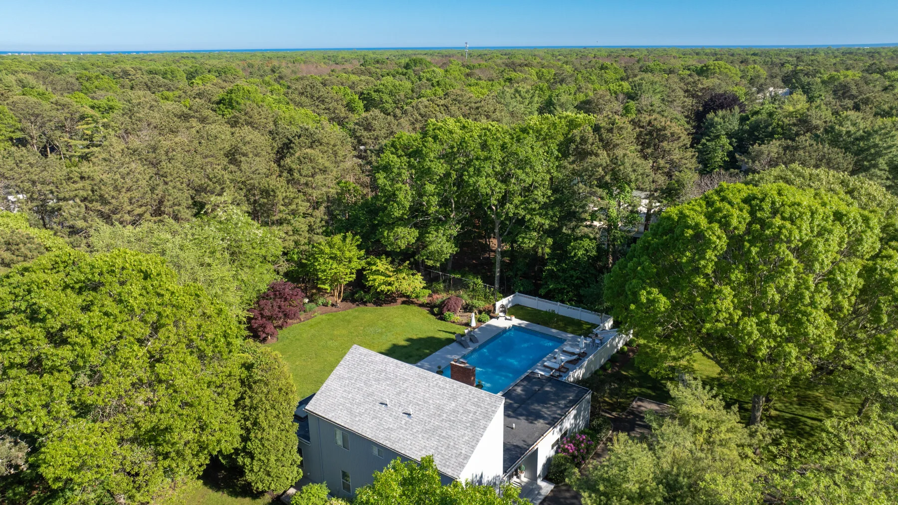 Aerial view of a swimming pool beside a house, surrounded by trees.