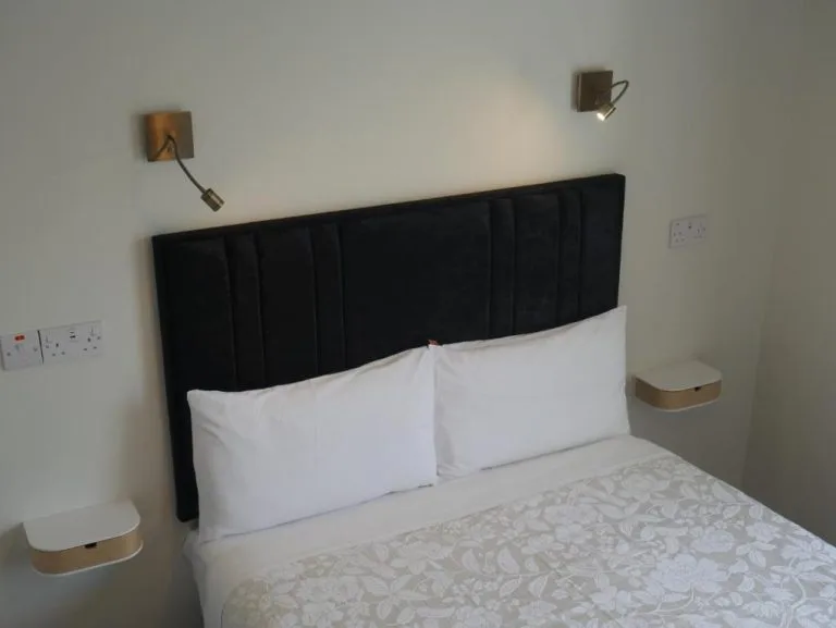 Espacio representativo del hotel: Un dormitorio con una cama, almohadas blancas y un cabecero oscuro tapizado.