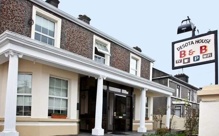 Espacio representativo del hotel: La fachada de ladrillo de un hotel tiene una entrada con columnas blancas y un letrero encima.