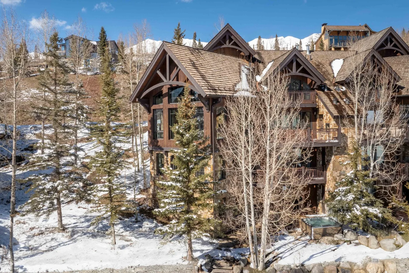 A large timber lodge stands among snow-dusted trees beneath a clear blue sky.