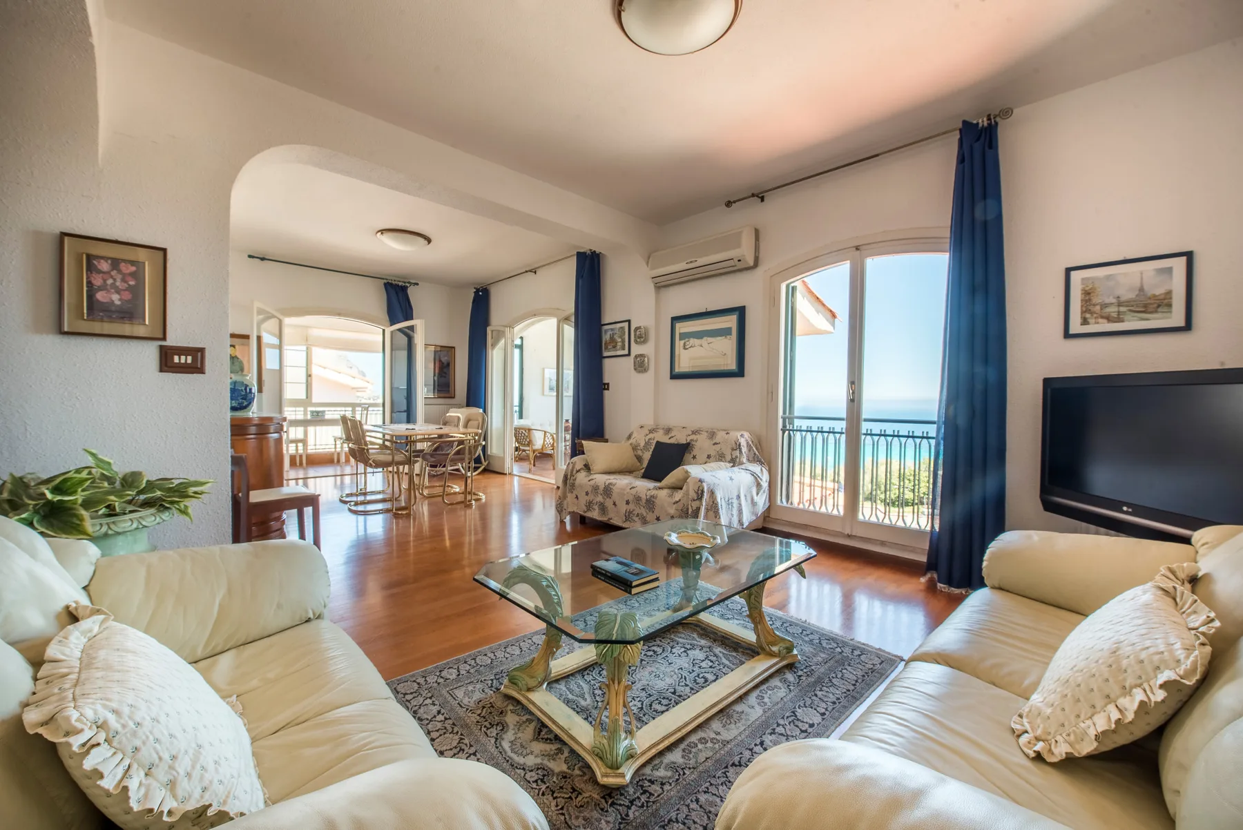 A bright living room with seating around a glass coffee table and balcony doors.