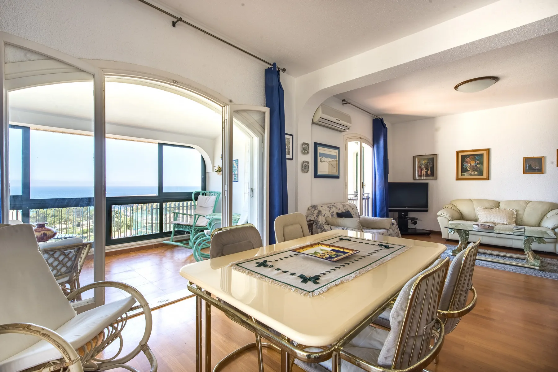 A living and dining room with a table, seating, and large windows opening onto a balcony.