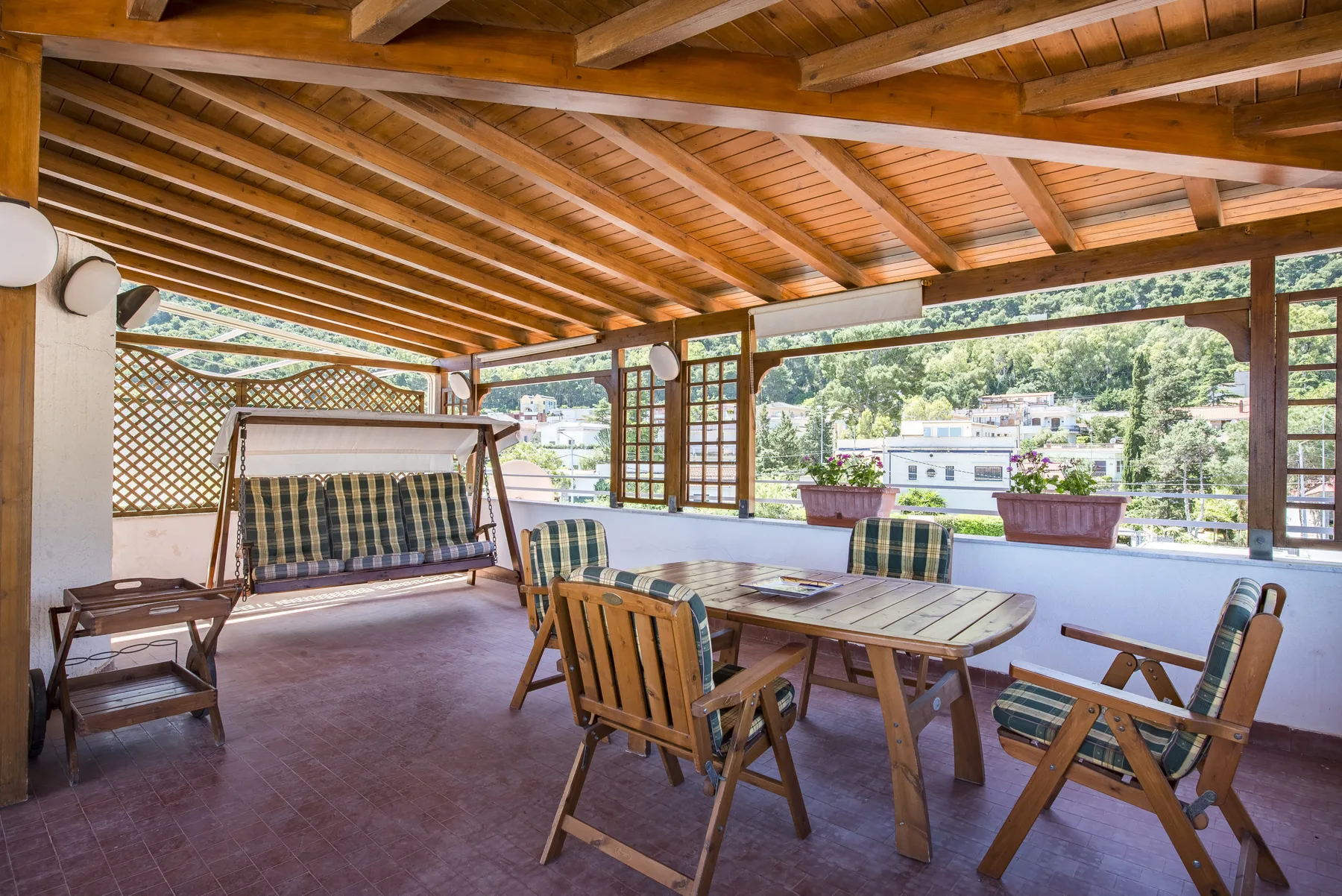 A covered wooden patio with a dining table and seating overlooks greenery.